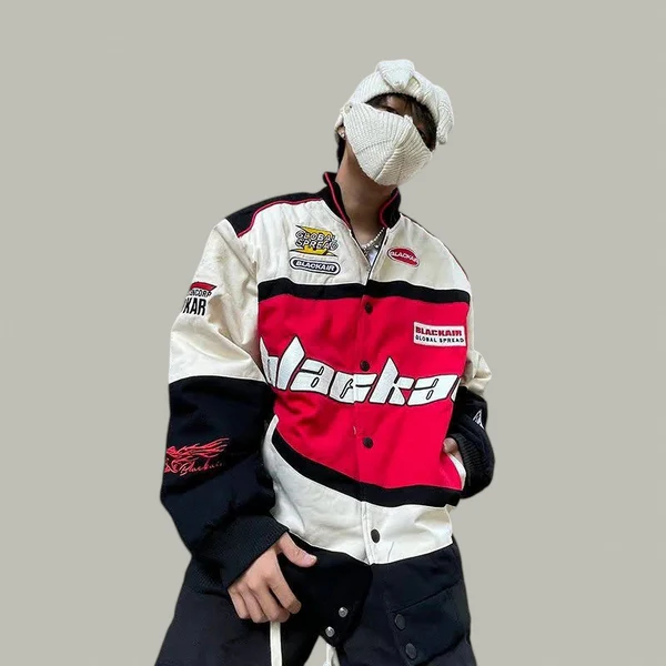 Person wearing a bold red, white, and black racing-style jacket with a covered face and streetwear pants, posing confidently against a plain background.