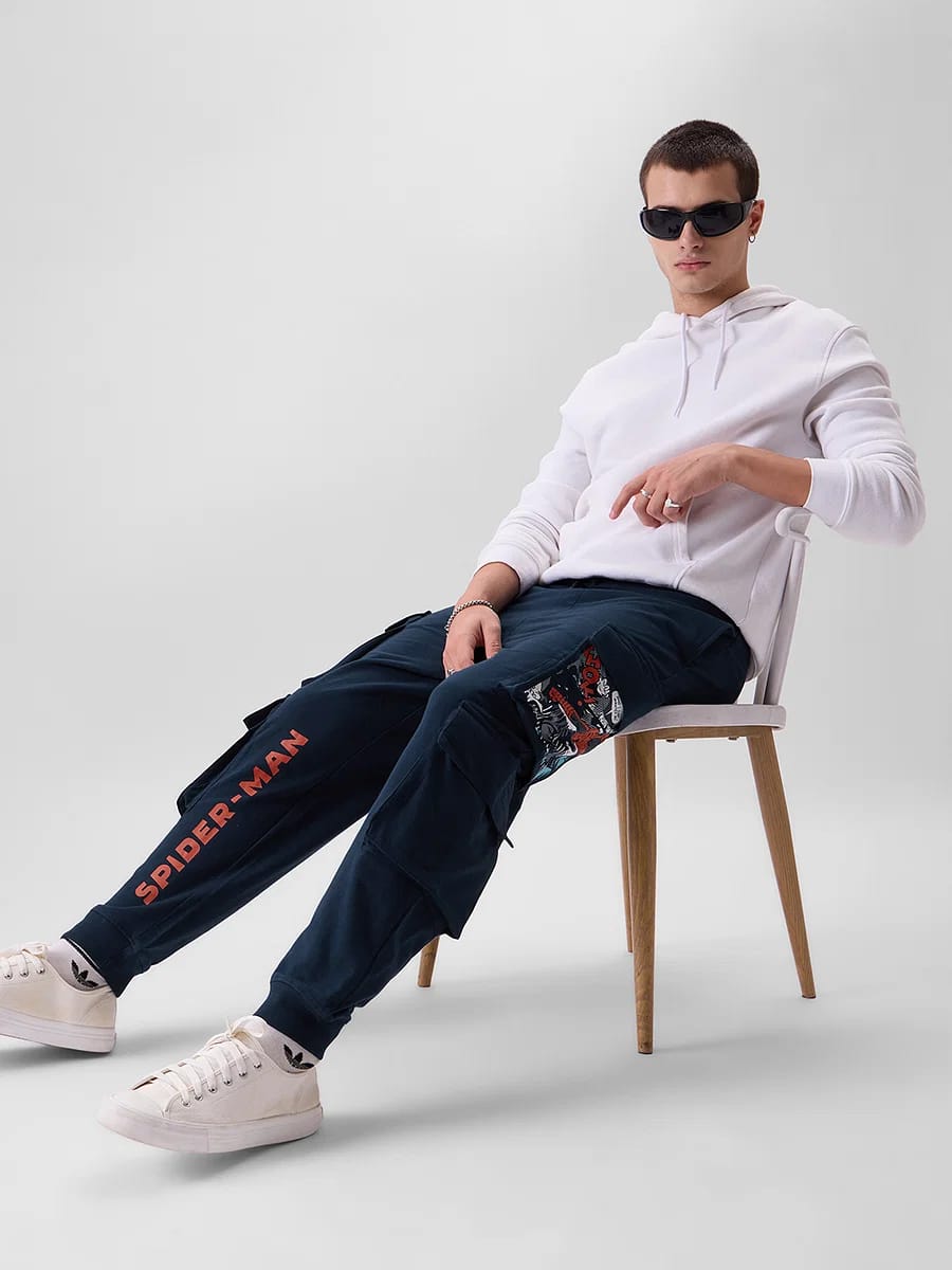 Model sitting in white hoodie and navy blue Spider-Man graphic joggers with cargo pockets